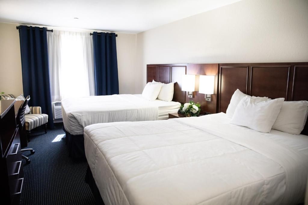 Bright hotel room with two double beds and dark curtains.