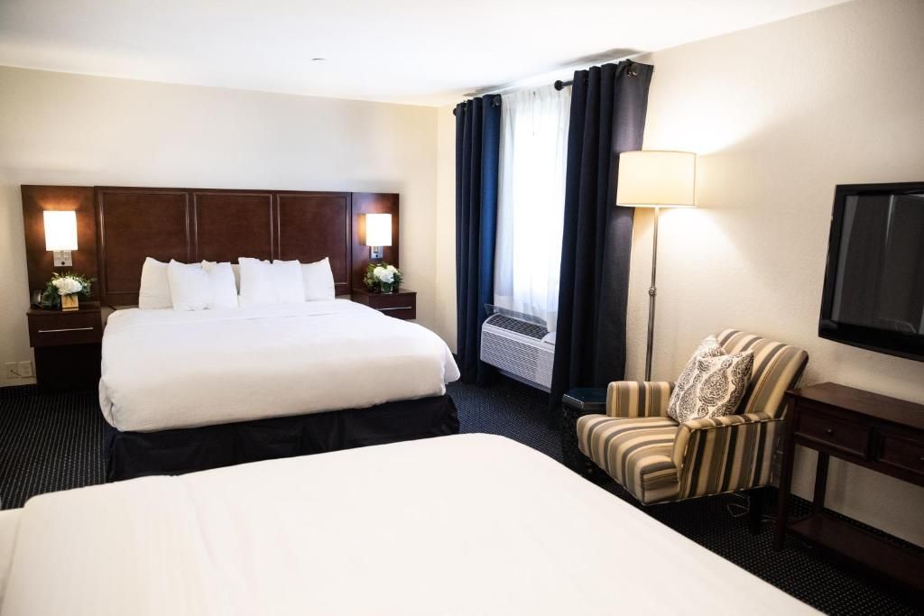 Cozy hotel room with two beds, a striped armchair, and a floor lamp.
