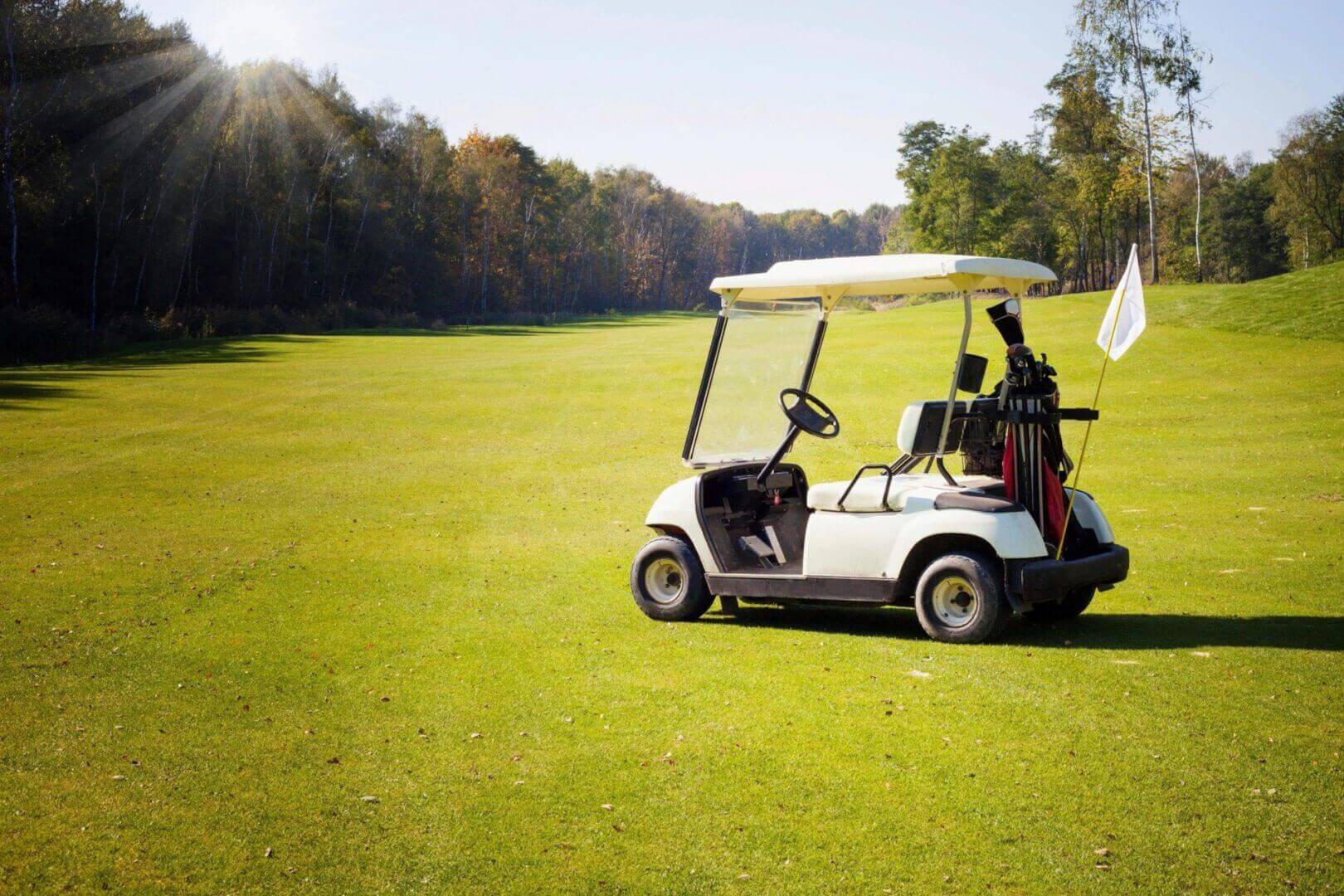 A golf cart parked on a green golf course under clear skies.